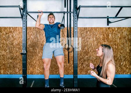 Young female athlete training and helping handicapped sportsman on horizontal bar during training in gym Stock Photo
