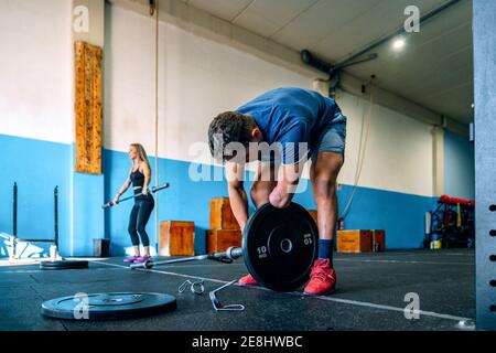 Disabled male athlete leaning forward while putting plate on bar near sportsWoman working out in gym Stock Photo