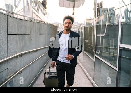 African American male tourist with suitcase running in airport while hurrying for flight and looking forward Stock Photo