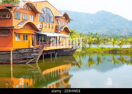 Tropical landscape. Wooden house in the form of a boat on the ocean with a view of the mountains. Travel and tourism in Asia. Stock Photo