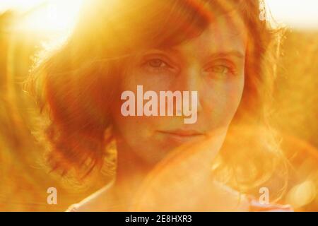 Crop thoughtful adult female resting in nature and looking at camera pensively under bright sunlight during golden hour Stock Photo