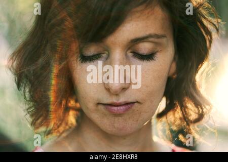 Crop thoughtful adult female resting in nature and looking down pensively under bright sunlight during golden hour Stock Photo