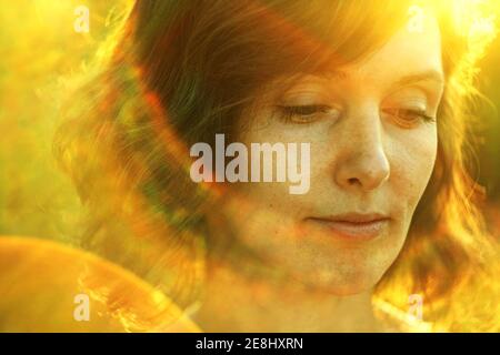 Crop thoughtful adult female resting in nature and looking down pensively under bright sunlight during golden hour Stock Photo