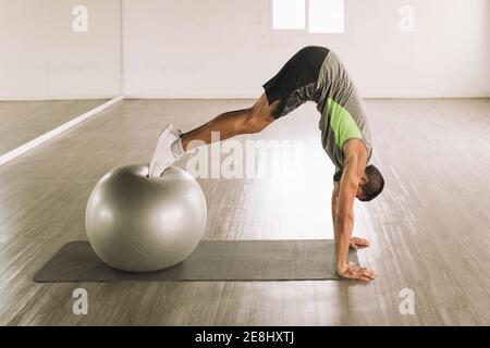 Side view of unrecognizable young muscular male athlete in sportswear performing Swiss Ball Pike exercise on mat during workout in studio Stock Photo