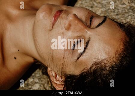 From above of crop peaceful young female sunbathing with closed eyes while lying on sandy beach Stock Photo