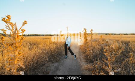 Side view of active young lady in trendy outfit dancing in dry fiends against cloudless blue sky in countryside Stock Photo