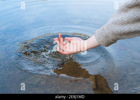 Cropped unrecognizable female traveler touching pure lake water from shore Stock Photo