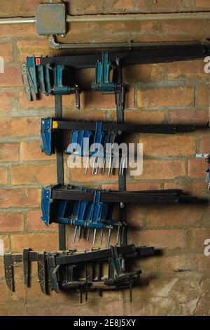 Collection of shabby carpentry clamps placed on metal racks on brick wall in woodworking workshop Stock Photo