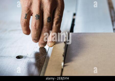 Closeup of crop unrecognizable male joiner cutting wood with circular saw in joinery Stock Photo