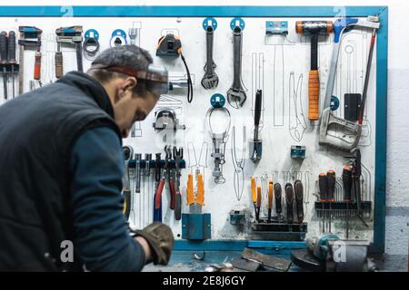 Side view of young male auto master screw part of motorcycle crankshaft bearing with wrench while working at table with various tools in garage Stock Photo