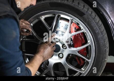 Crop anonymous male mechanic checking the condition of the car wheel during car maintenance in garage Stock Photo
