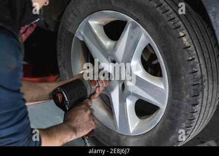 Crop anonymous male mechanic using automatic screwdriver while changing wheels during car maintenance in garage Stock Photo