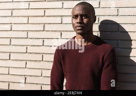 Serious young African American male standing while looking away in sunlight near billet wall Stock Photo