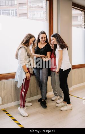 High angle of young smiling female dancers gathering in hall and watching video of dance on smartphone after lesson Stock Photo