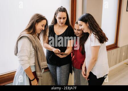 High angle of young smiling female dancers gathering in hall and watching video of dance on smartphone after lesson Stock Photo
