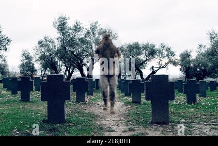 Anonymous soldier in camouflage carrying warrior backpack walking in spacious military cemetery Stock Photo