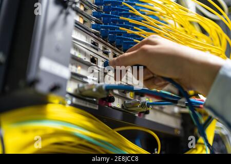 From below of crop anonymous man putting electronic cable in data system in communications room Stock Photo