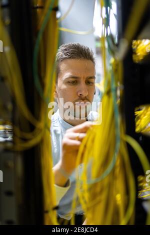 Concentrated male specialists working with wires in server while managing network in data center Stock Photo