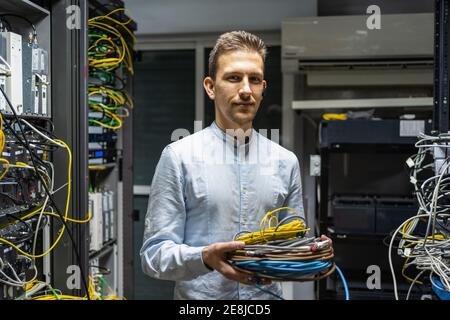 Smiling man in wireless headset standing with cables in network server room for providing Internet and communication Stock Photo