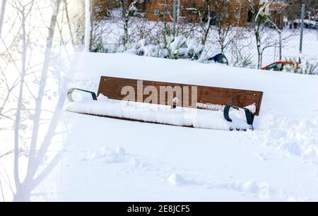 Empty bench made of wooden and metal material covered with white snow in town Stock Photo