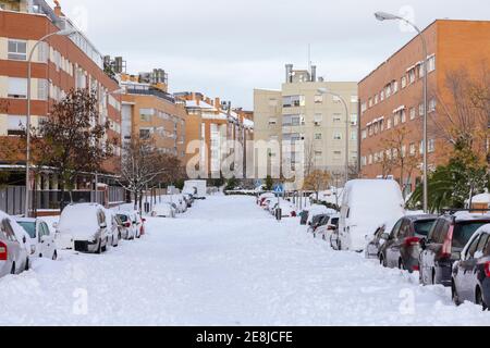 Rows of transport parked between snowy road and residential house facades under cloudy sky in winter city Stock Photo