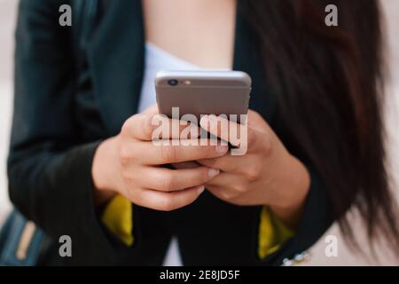 Cropped unrecognizable female entrepreneur in smart casual style standing in street of downtown browsing on mobile phone Stock Photo