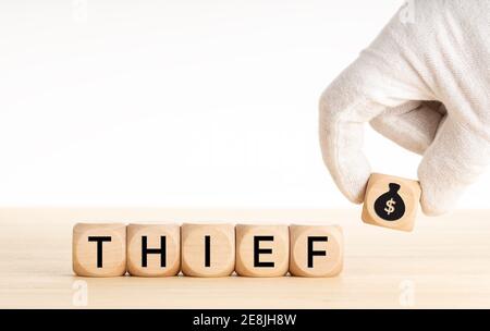 Thief concept. Hand picking a wooden block whit money bag icon and text on wooden dice. Copy space. White background Stock Photo