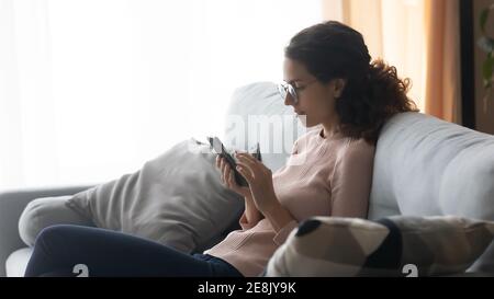 Relaxed young woman in glasses using mobile applications at home. Stock Photo