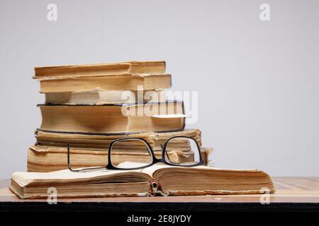 stack of old books with bookmarks on wooden table. glasses lie on an open book. Stock Photo