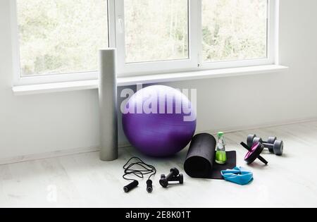 Empty modern white bright room with home workout accessories equipment. Yoga ball, resistance exercise latex band, foam roller, weights, jump rope. Stock Photo