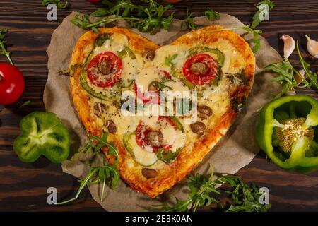 Pizza in the shape of a heart  and fresh vegetables on a dark wooden background. Stock Photo