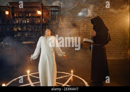 Exorcist in hood casting out demons from a woman Stock Photo