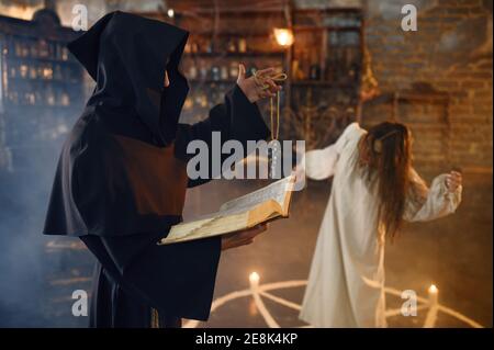 Exorcist in hood casting out demons from a woman Stock Photo