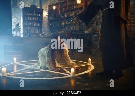 Exorcist in hood casting out devil from a woman Stock Photo