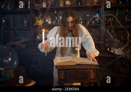 Demonic woman with candle reads book of spells Stock Photo