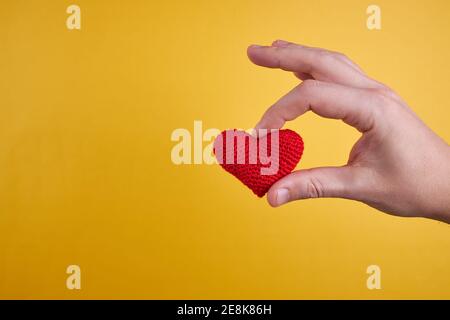 male person hold wool heart in his hand isolated on an yellow background. romance and valentine day concept Stock Photo