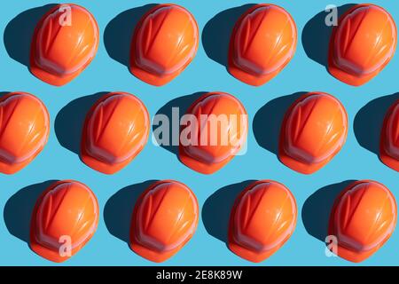 orange safety helmet rows on a blue background with hard shadows. looking from above.industrial pattern backdrop