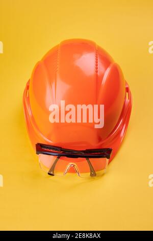 orange protective helmet and safety glasses near it on a bright yellow background. protective workwear and construction industry concept Stock Photo