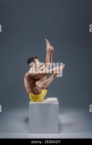 Male yoga sitting on the pedestal in studio, meditation position, grey