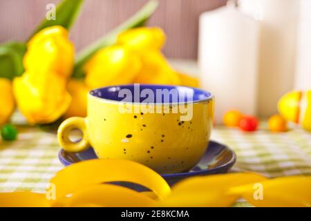 Easter table setting with white plate, basket of colorful eggs, candles and yellow tulips Stock Photo