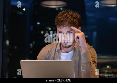 Young man analyst working until late hours by pc screen Stock Photo