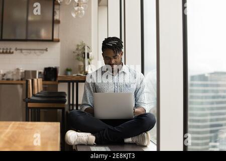 Concentrated african man sitting with crossed legs working on laptop Stock Photo