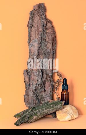 Dropper glass bottle of essential oil, tree bark, stone, dried plant on peach background Stock Photo