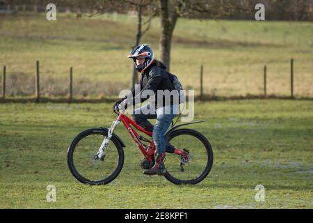 Hamilton, Scotland, UK. 31st Jan, 2021. Pictured: A downhill mountain biker cycles across the grass. People out in Chatelherault Country Park taking in exercise as the temperature stays just above freezing. The sun is out and people are enjoying themselves during the coronavirus phase 4 lockdown. Credit: Colin Fisher/Alamy Live News Stock Photo