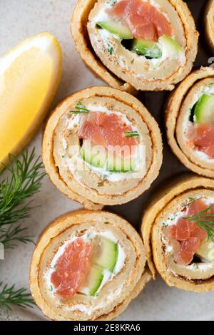 Crepe rolls with salmon, cucumber and cream cheese on a plate, top view