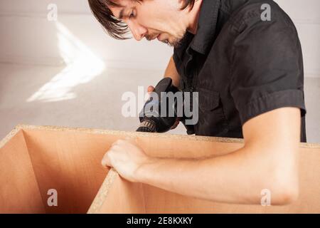 A man drills a hole in a closet using a drill. Stock Photo