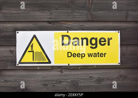 Danger deep water sign with icon in warning triangle, UK. Isolated on wooden planked background wall. Stock Photo