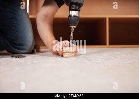 A man drills a hole in the wood against the background of an inverted closet on the white floor. Stock Photo