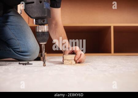 A man drills a hole in the wood against the background of an inverted closet on the white floor. Stock Photo