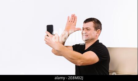 Smiling man sitting in a chair communicates by video using gestures and shows a sign means dad. White background. Non verbal influencer Stock Photo